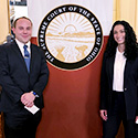 A smiling man and a woman stand next to a graphic showing the seal of the Supreme Court of Ohio